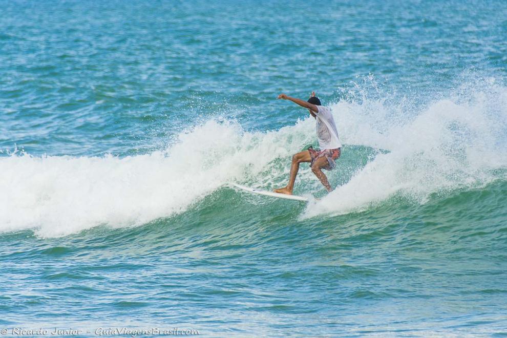Imagem de um surfista de braços abertos em cima da onda.